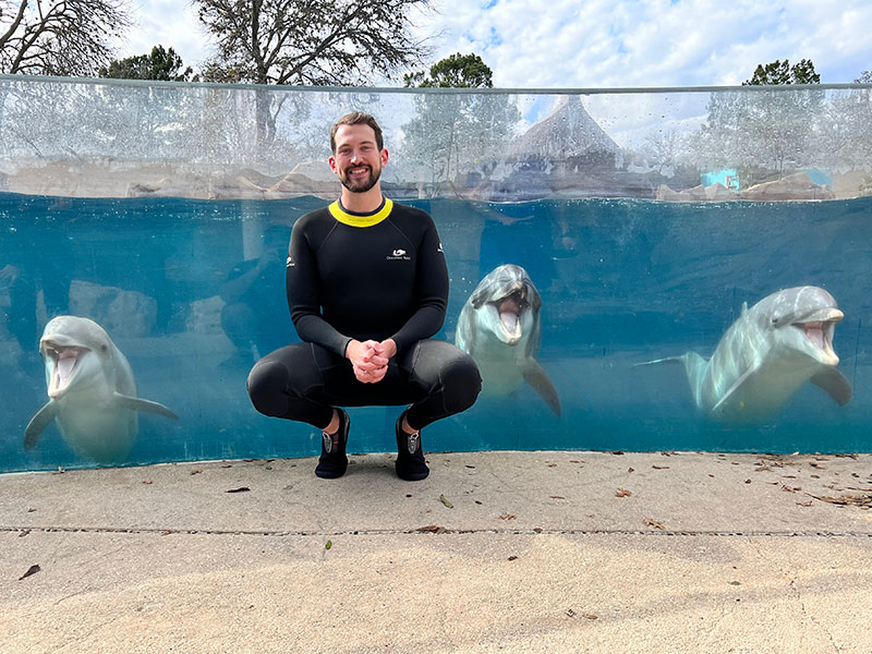 brock crockett-beck poses with dolphins during his SeaWorld externship