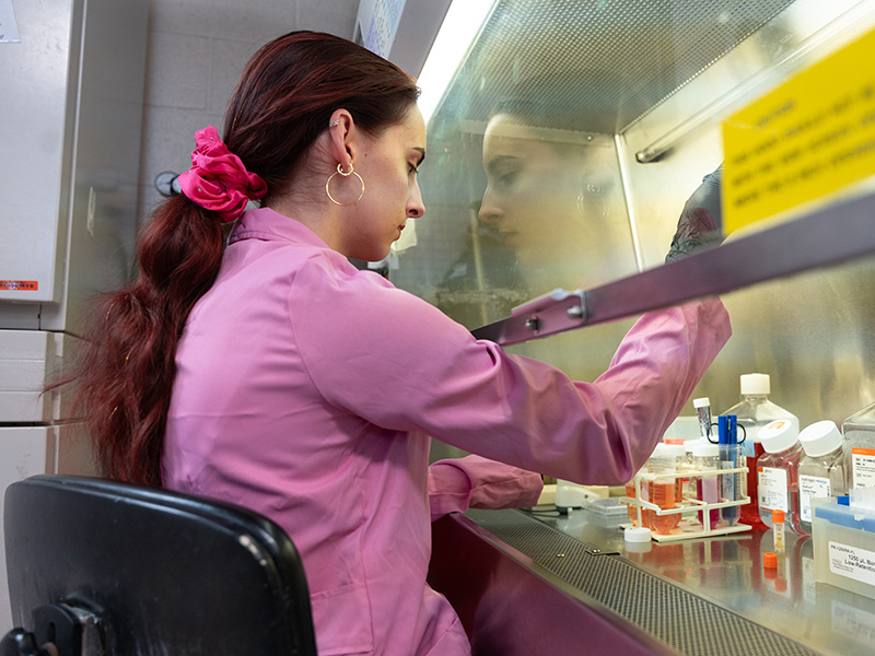 A woman in a pink labcoat uses a pipette in a lab setting